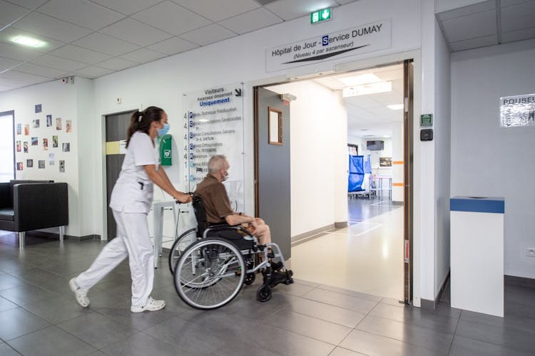 Photo illustrant une professionnelle de santé en train d'emmener un patient en fauteuil roulant dans le bon service de la clinique des minimes